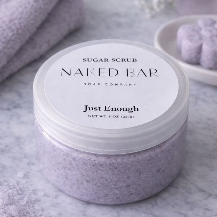 Naked Bar Soap Co. Emulsified Sugar Scrub container on a marble surface with a towel and bottle in the background